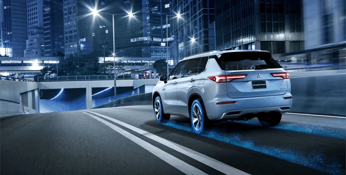 Vue 3/4 arrière du Mitsubishi Outlander PHEV 2025 conduisant sur une route en ville.