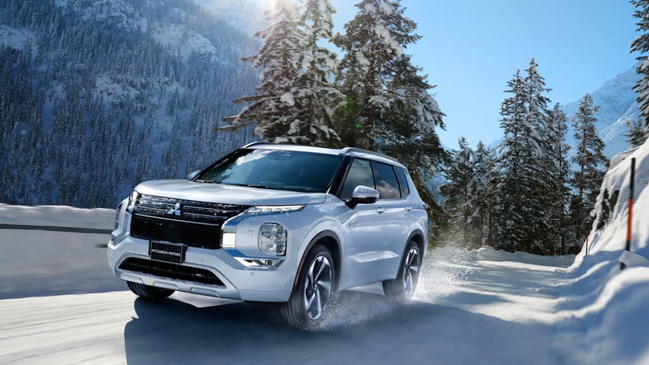 vue latérale avant d'une Mitsubishi Outlander PHEV 2024 sur une route de montagne eneigée